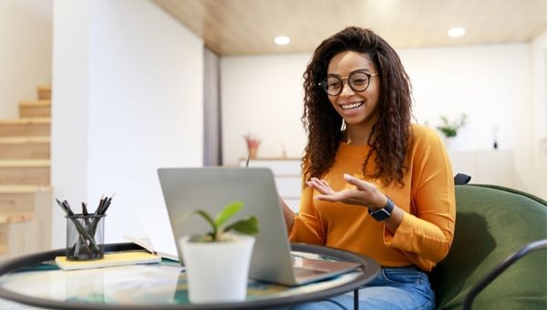 Foto van een vrouw met een bril. Ze kijkt blij en gebaart naar haar laptop.